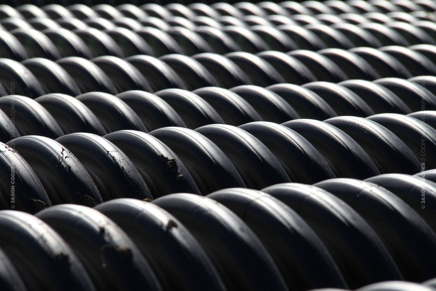 photos of a stack of corrugated black pipe in a construction area